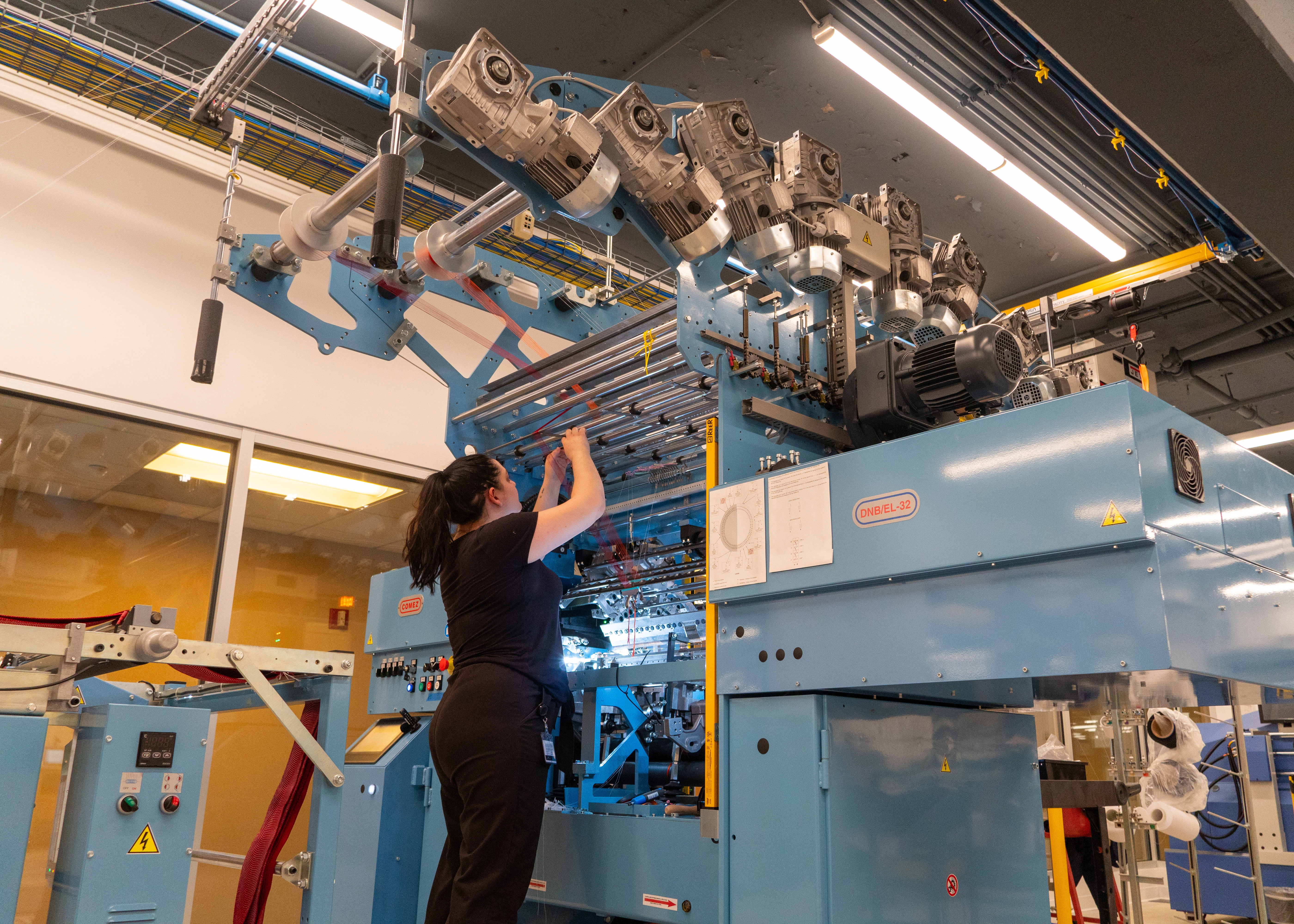 A person reaching upwards to operate a large warp knitting machine